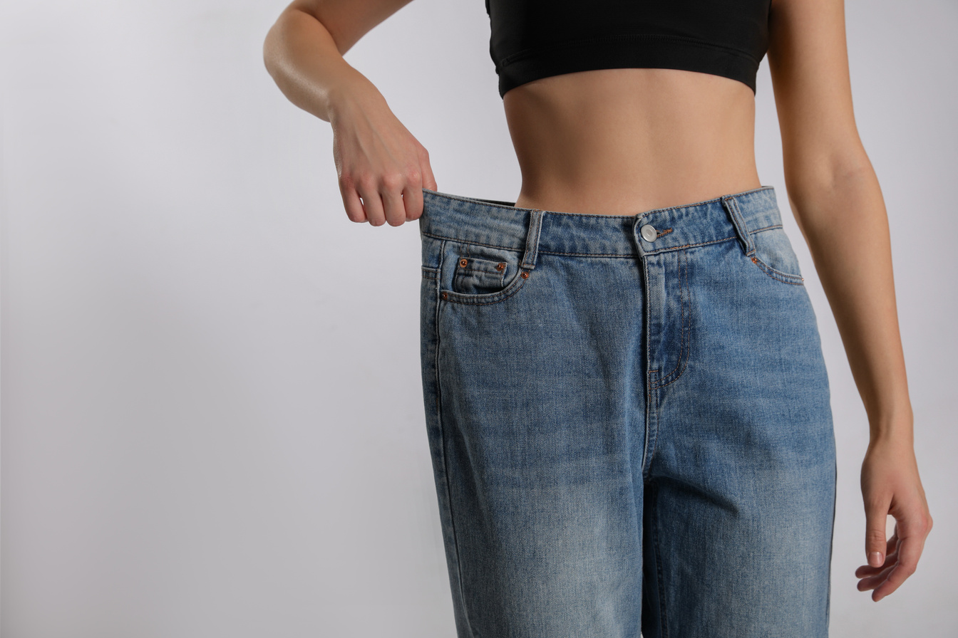 Skinny Woman in Oversized Jeans on Light Background, Closeup Wit